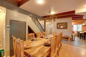 A dining area with a wooden table set for a meal, surrounded by chairs, and a staircase leading to an upper level. - Near Heavenly & Lake Tahoe! Mountain Home, Hot Tub (South Lake Tahoe)