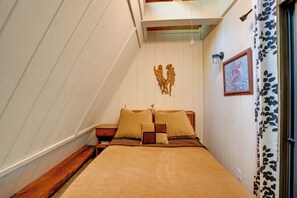 Ein Schlafzimmer mit schrägen Wänden, einem Bett mit zwei Kissen, einem Nachttisch und einer an der Wand befestigten Leuchte.