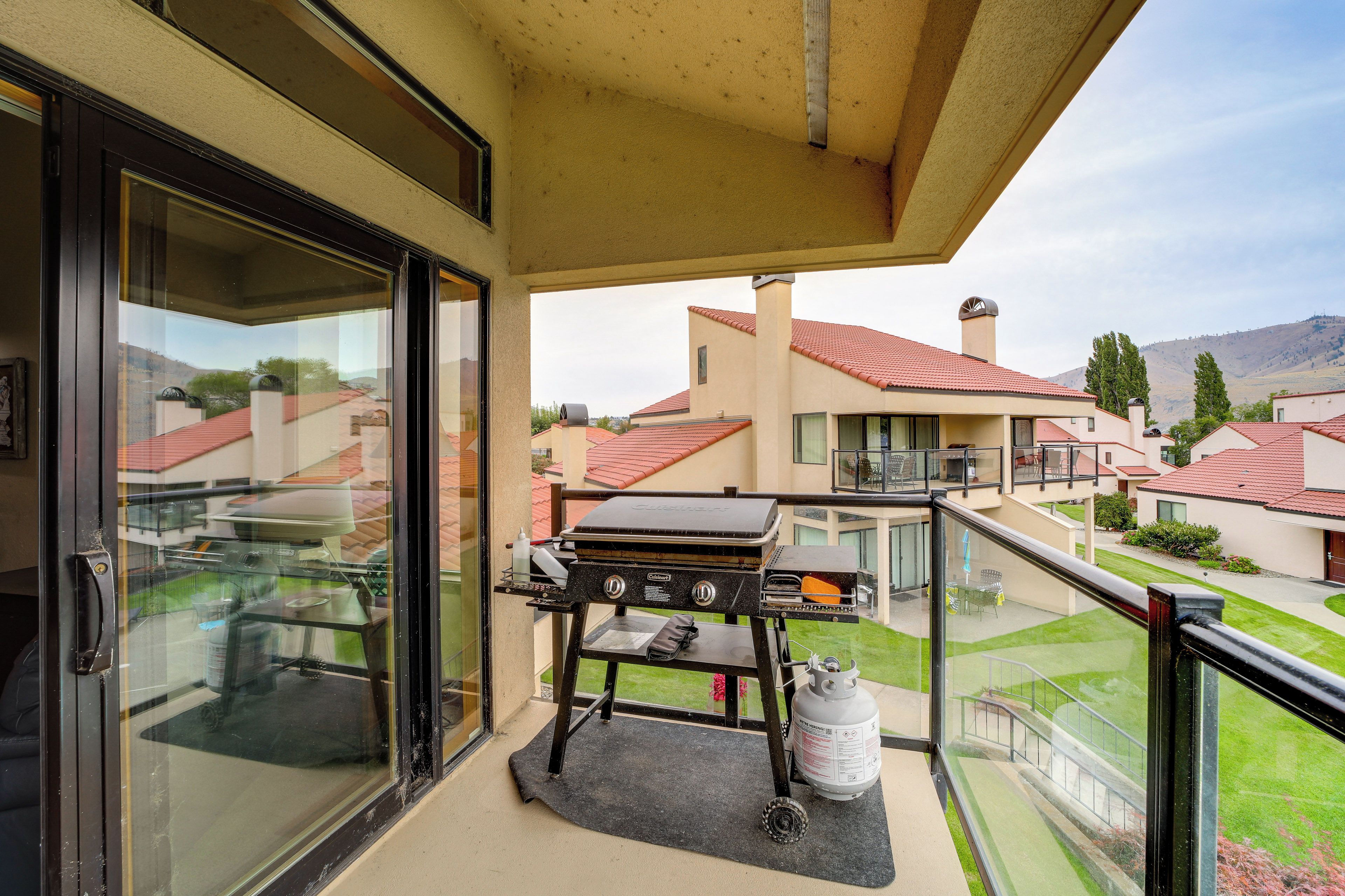 A balcony with a grill, a gas cylinder, and a view of neighboring houses.