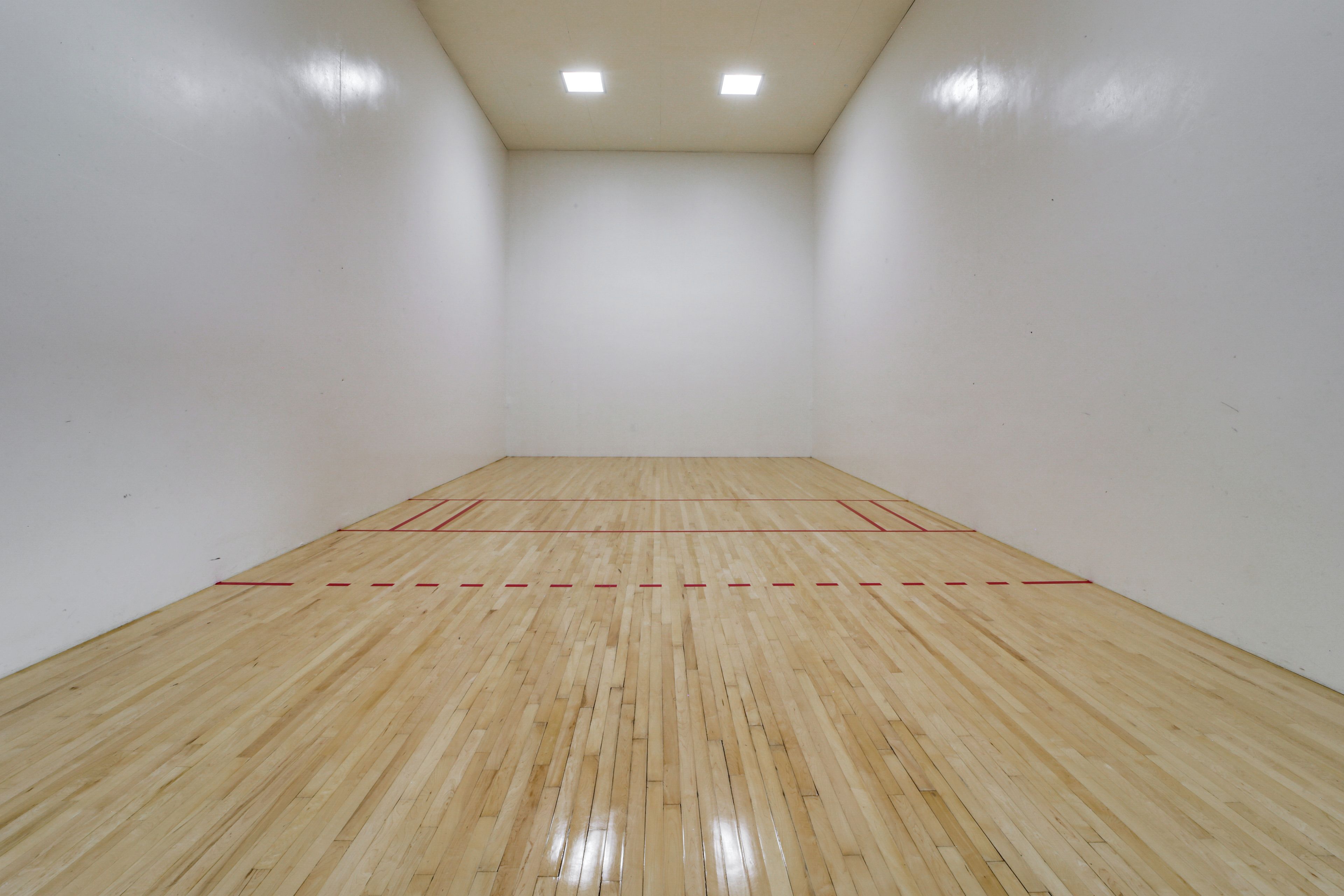 A squash court with wooden flooring and red boundary lines.