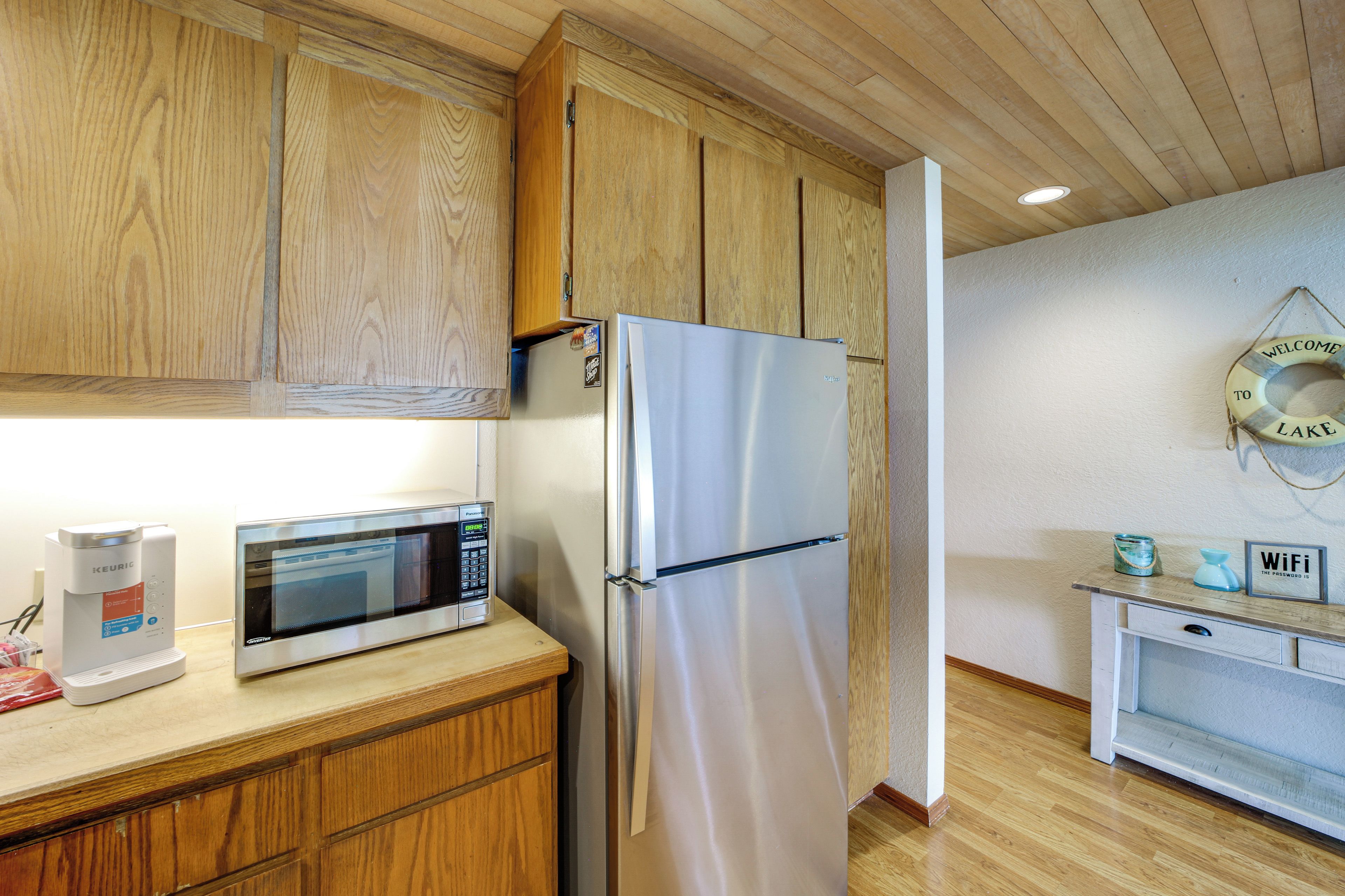A compact kitchen with wooden cabinets, a stainless steel refrigerator, a microwave, and a small countertop with a coffee maker.