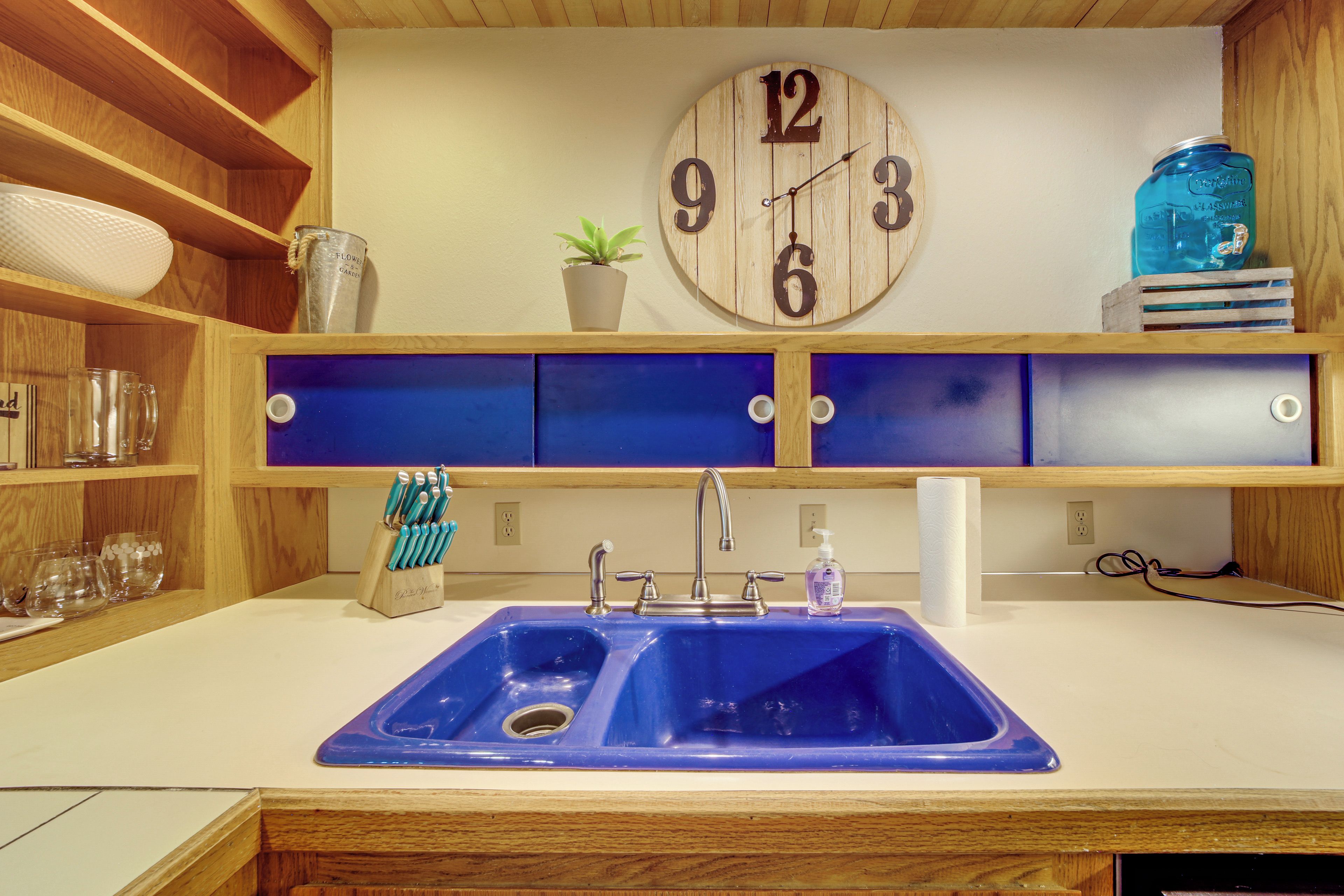 A kitchen with a wooden clock, a sink, and shelves with glassware.