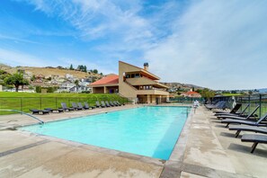A swimming pool with lounge chairs, a building with a red roof, and a hilly landscape in the background.