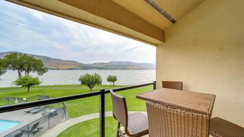 A balcony with a view of a lake and mountains, furnished with wicker chairs and a table.