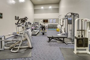 Academia com máquinas de cardio, equipamentos de musculação e área de piscina ao fundo.