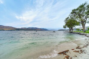 Un lago con aguas cristalinas, una playa de arena y un árbol a la derecha.