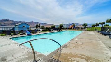A swimming pool with a metal ladder, lounge chairs, and a playground with a slide.