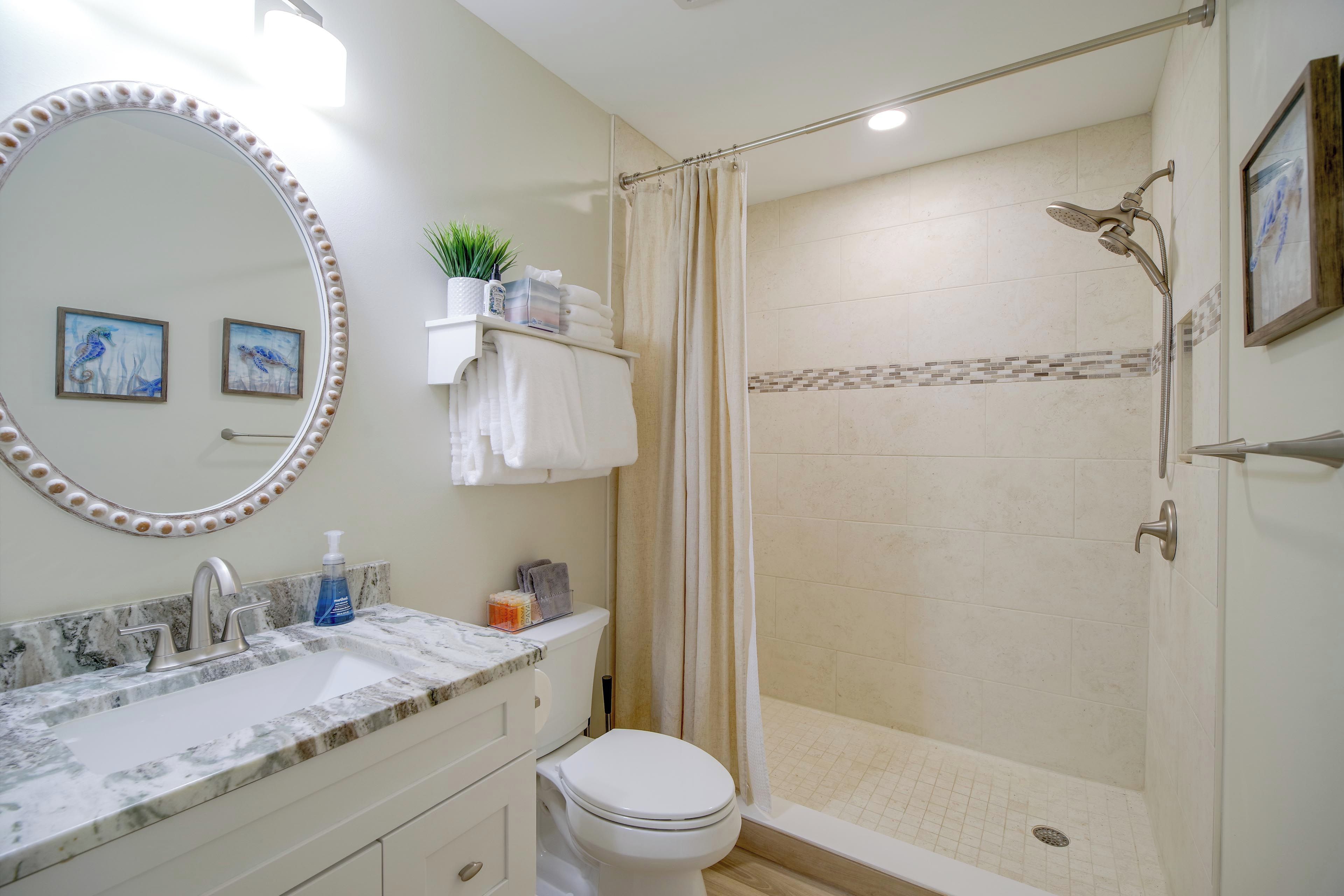 A bathroom with a marble sink, a toilet, a shower with a glass door, and a large mirror with lights.