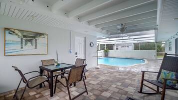 Un patio techado con piscina, mobiliario exterior y un cuadro en la pared.