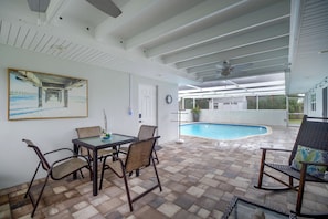 A covered patio area with a pool, outdoor furniture, and a painting on the wall.