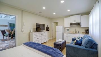 A modern bedroom with a bed, a television, a dresser, and a kitchenette.