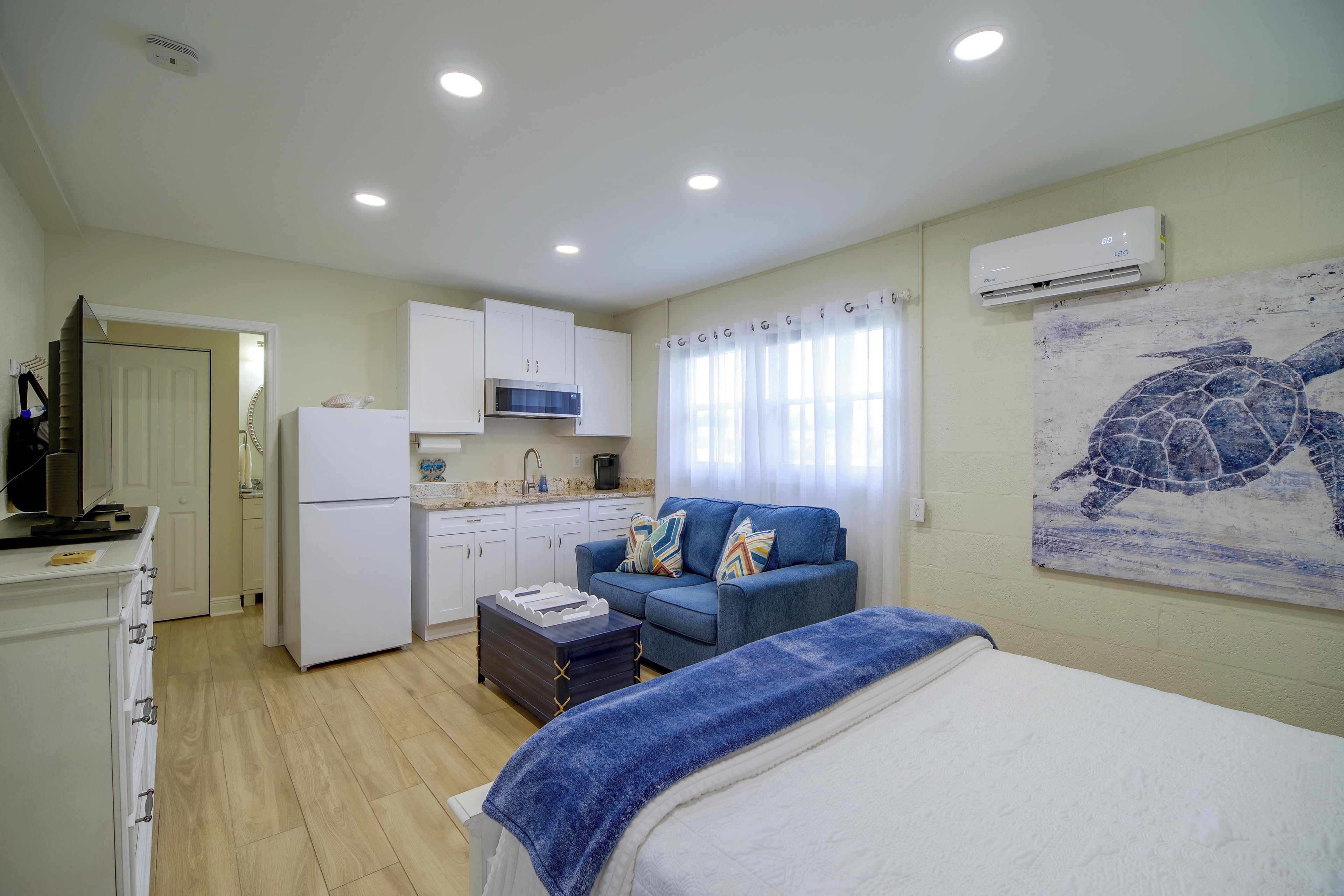Un espacio habitable compacto con kitchenette, una cama con manta azul y un mural de una tortuga en la pared.