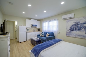 A compact living space with a kitchenette, a bed with a blue blanket, and a turtle mural on the wall.