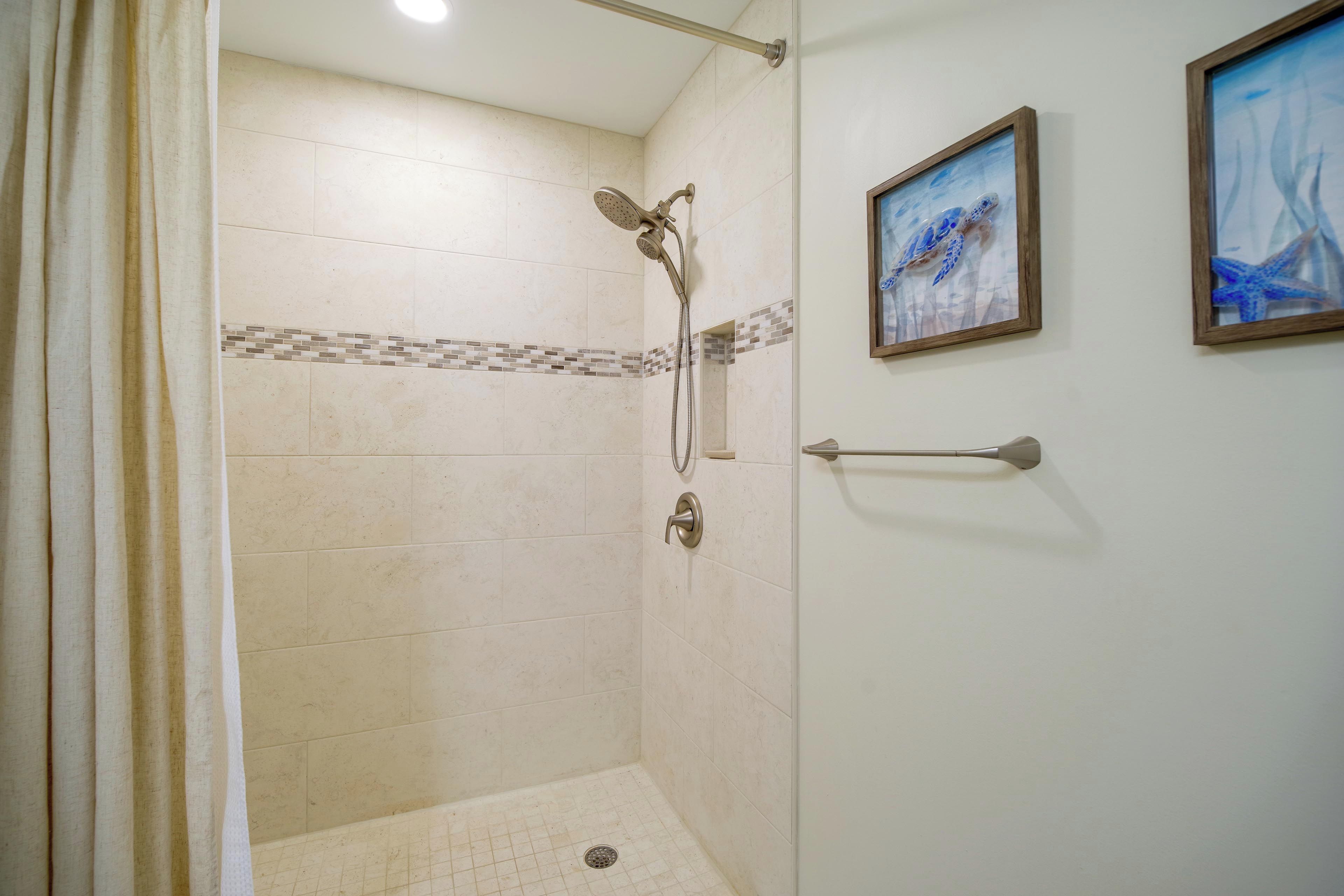A shower with a handheld showerhead, a glass door, and a tiled floor.
