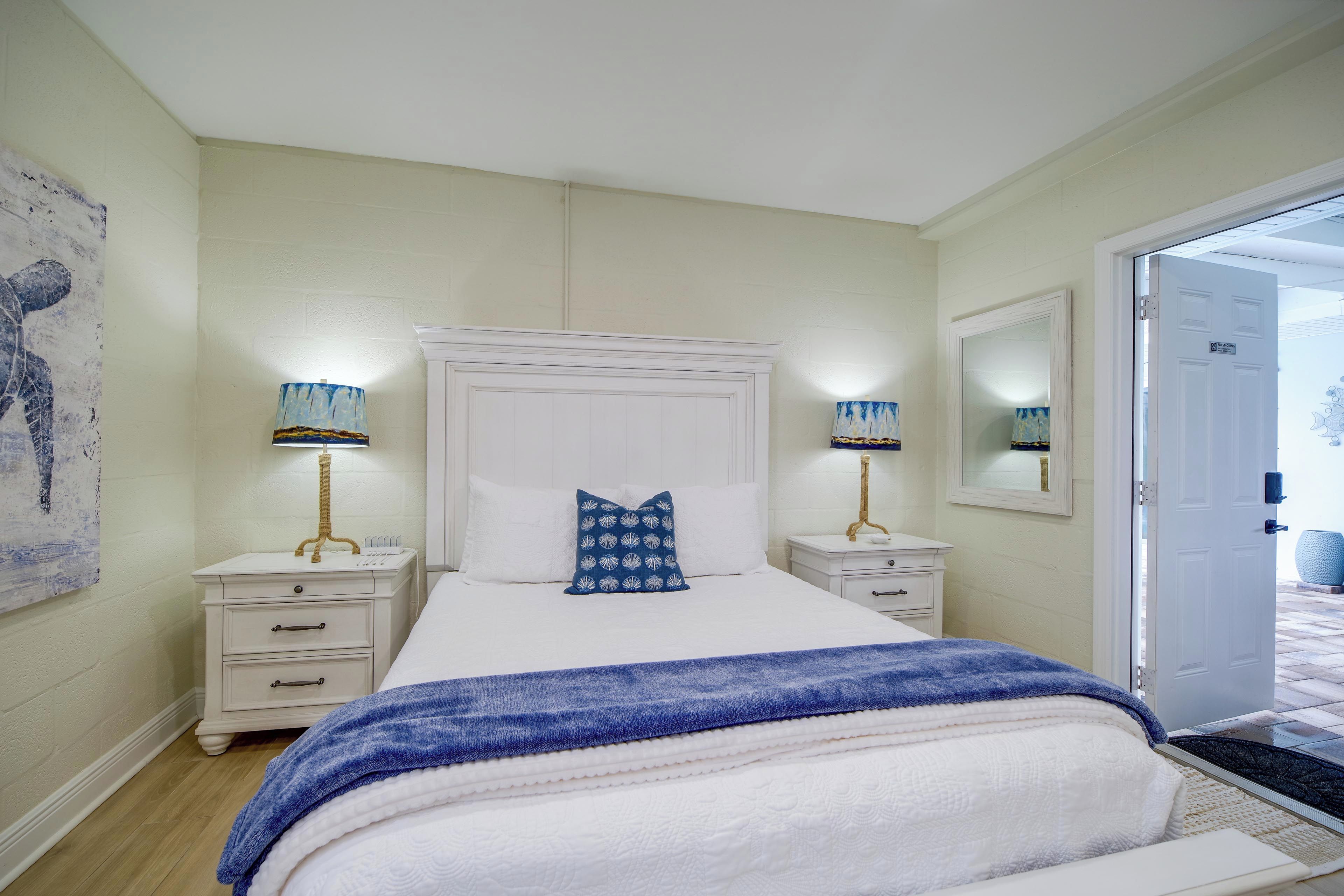 A bedroom with a bed, two bedside tables, a nightstand, a large mirror, and a door.