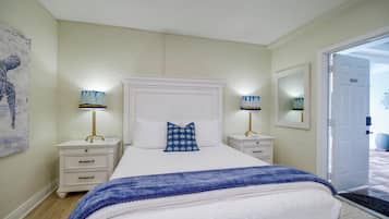 A bedroom with a bed, two bedside tables, a nightstand, a large mirror, and a door.