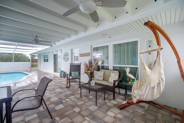 A covered patio area with a pool, outdoor furniture, and a hammock.