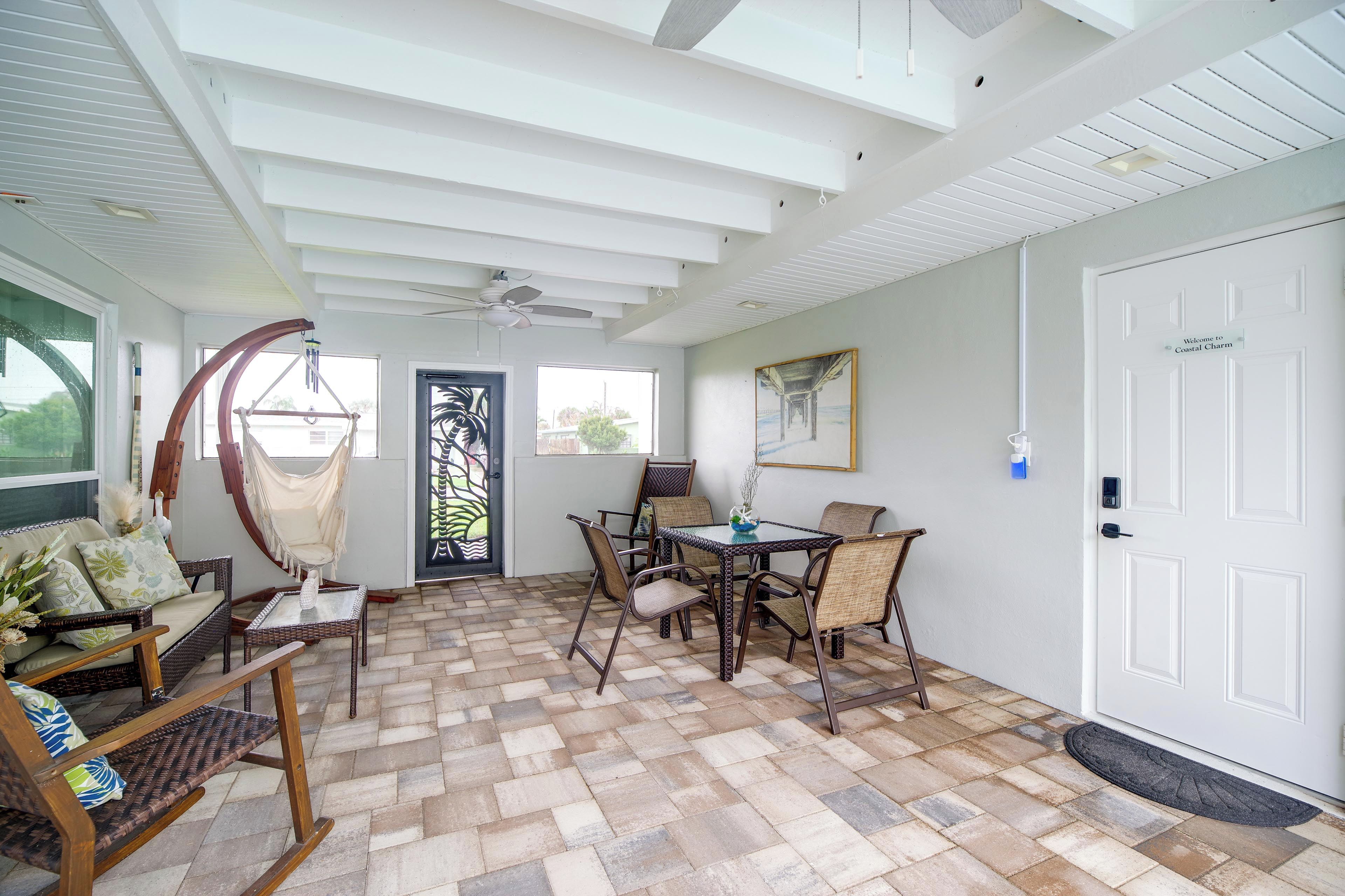 A room with a dining table, chairs, a hammock, and a door with a welcome sign.
