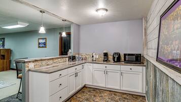 A kitchen with white cabinets, a granite countertop, a coffee maker, a microwave, and pendant lighting.