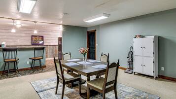 A dining area with a wooden table set for four, surrounded by chairs, a vase of flowers, and a kitchen area with cabinets and a refrigerator.