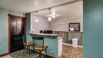A kitchen with a bar area, two chairs, a trash can, and a framed picture on the wall.
