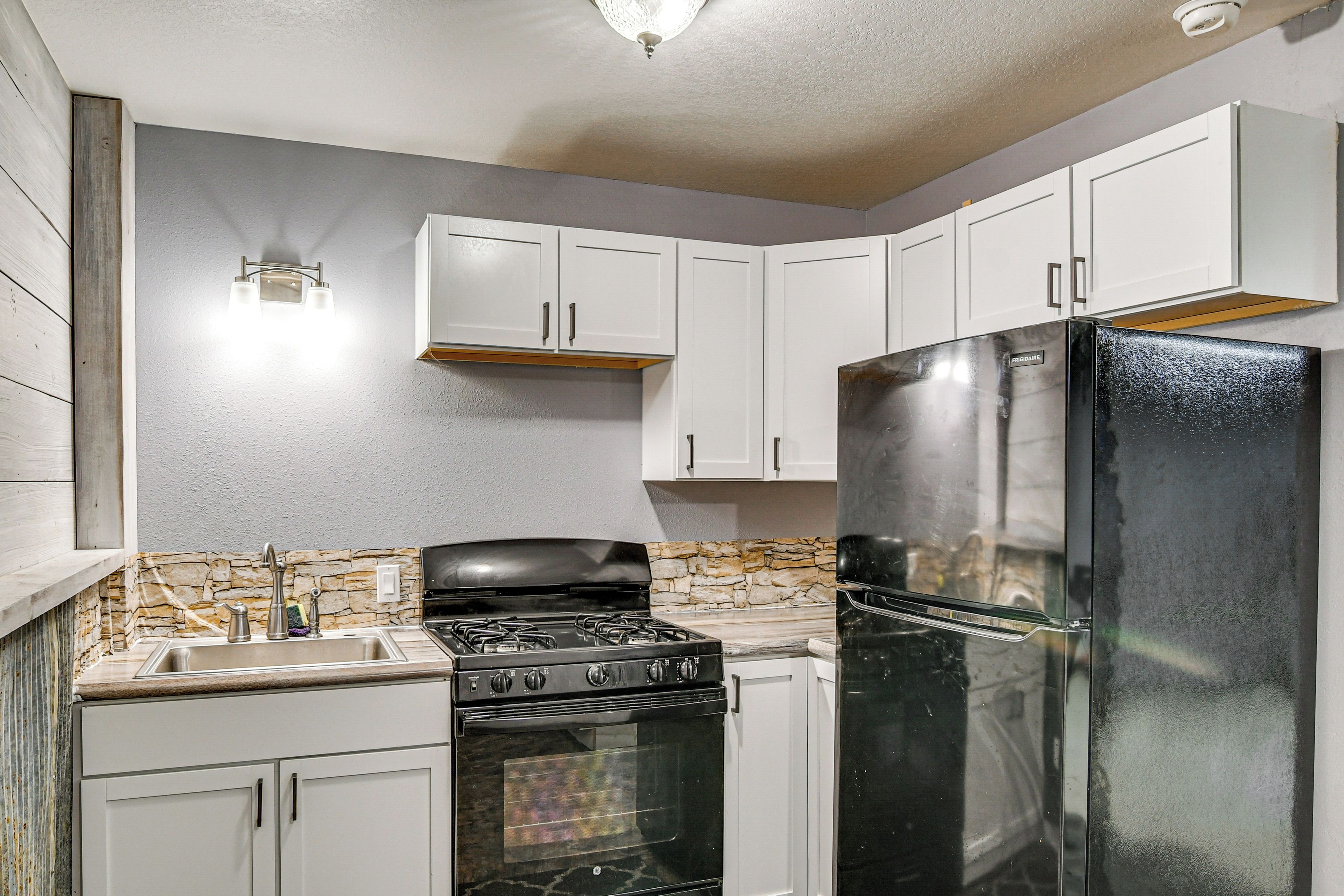 A kitchen with white cabinets, a black refrigerator, a stove, and a stone backsplash.
