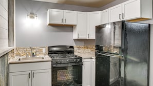 A kitchen with white cabinets, a black refrigerator, a stove, and a stone backsplash. - 9 Mi to Clear Lake! Cozy Apartment (Garner)