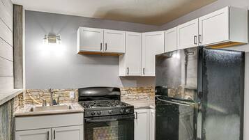 A kitchen with white cabinets, a black refrigerator, a stove, and a stone backsplash.