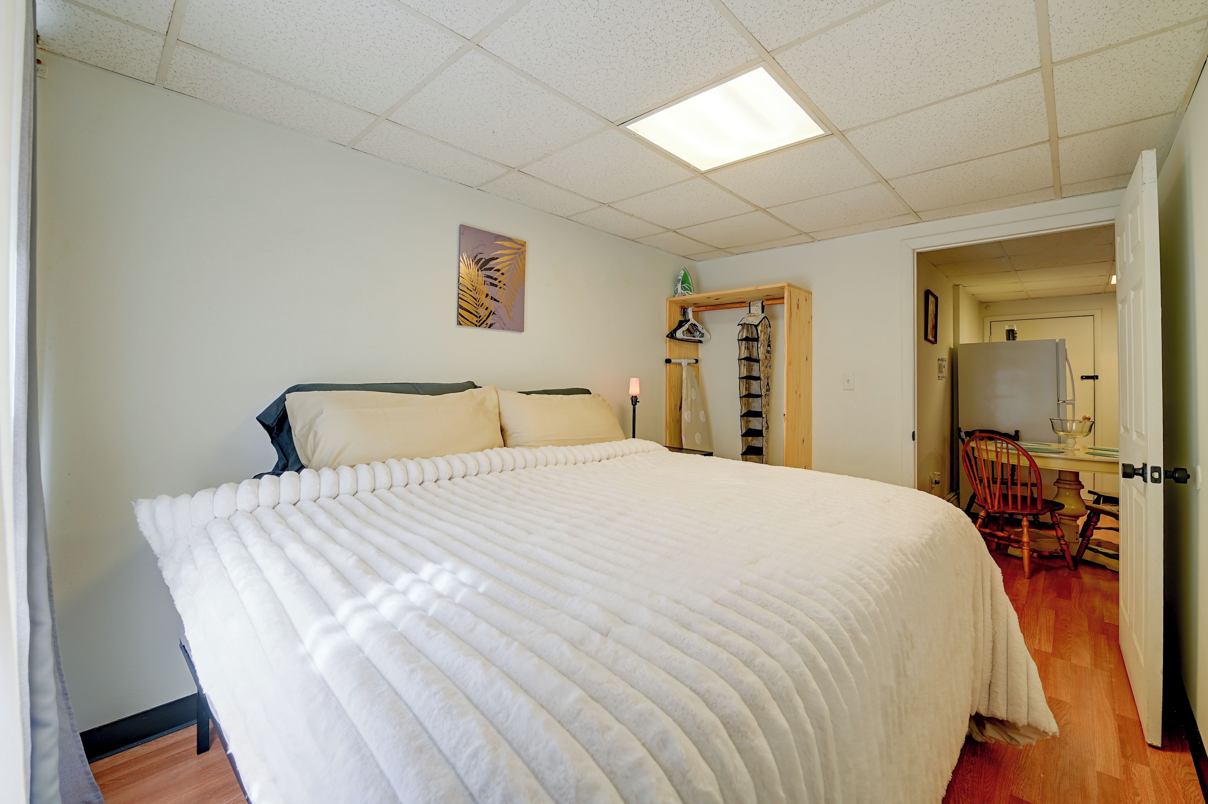 A bedroom with a large bed, a wooden chair, a desk with a chair, and a door leading to another room.