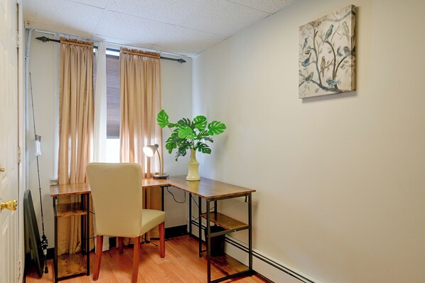 A room with a desk, chair, a potted plant, and a painting on the wall.