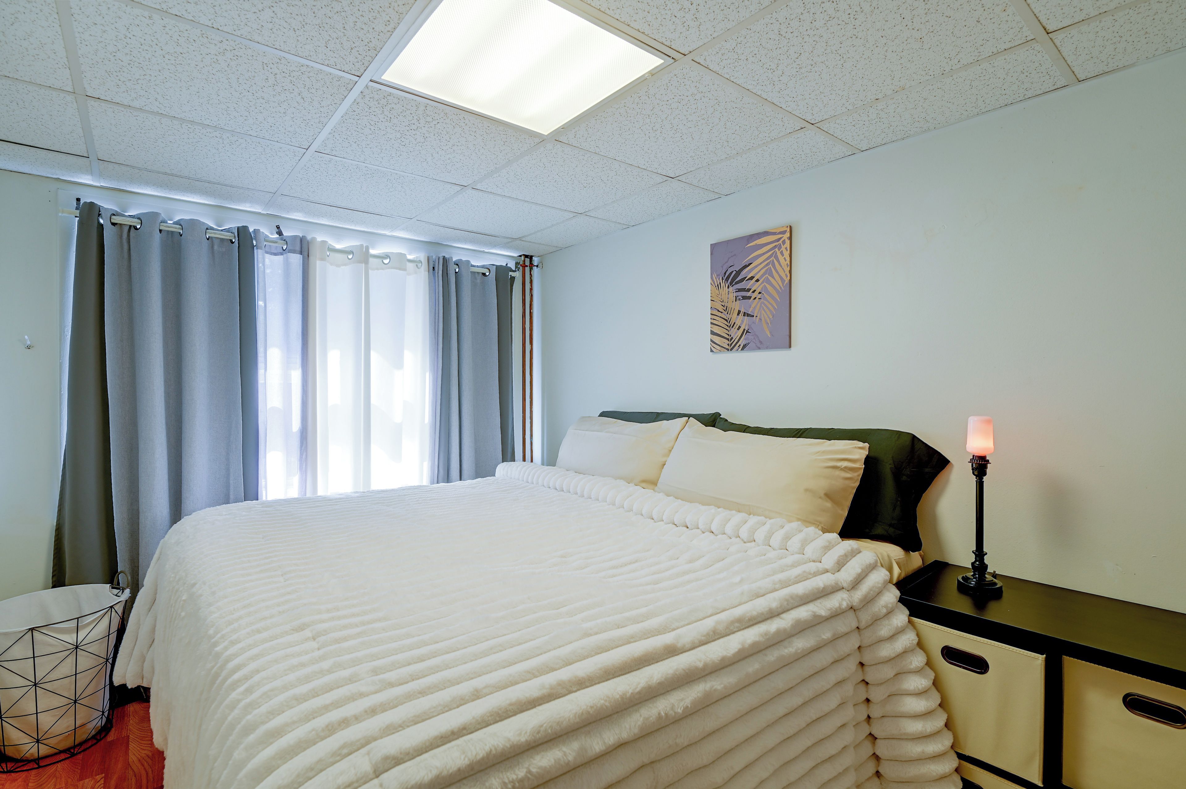 A hotel room with a bed, a nightstand, a lamp, a painting, and a window with curtains.