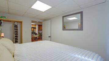 A bedroom with a bed, a mirror, and a kitchenette in the background.