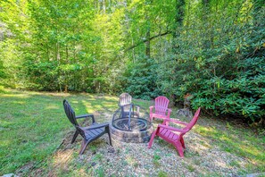 A circular fire pit with four chairs around it, set on a gravel area with grass and trees in the background. - Ski & Hike! Cozy Sapphire Retreat (Sapphire)