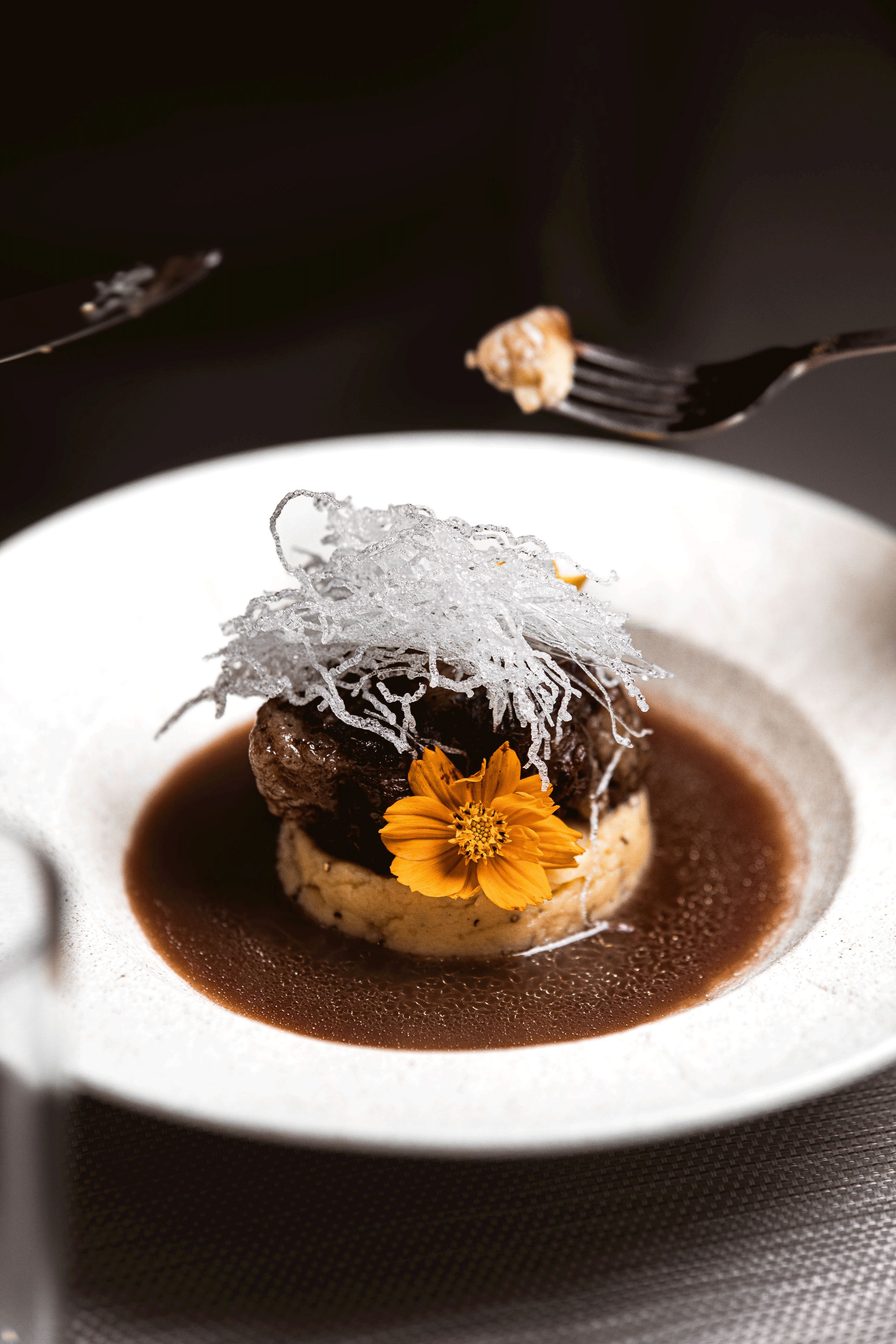 Un postre en un plato blanco con salsa oscura, una flor y lo que parece ser azúcar o cristales de azúcar.
