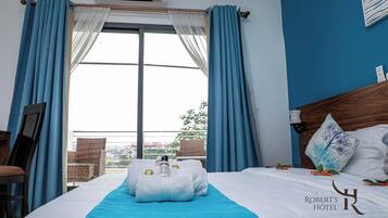Een hotelkamer met een bed, een raam met gordijnen, uitzicht op buiten, en een bord met de hotelnaam.