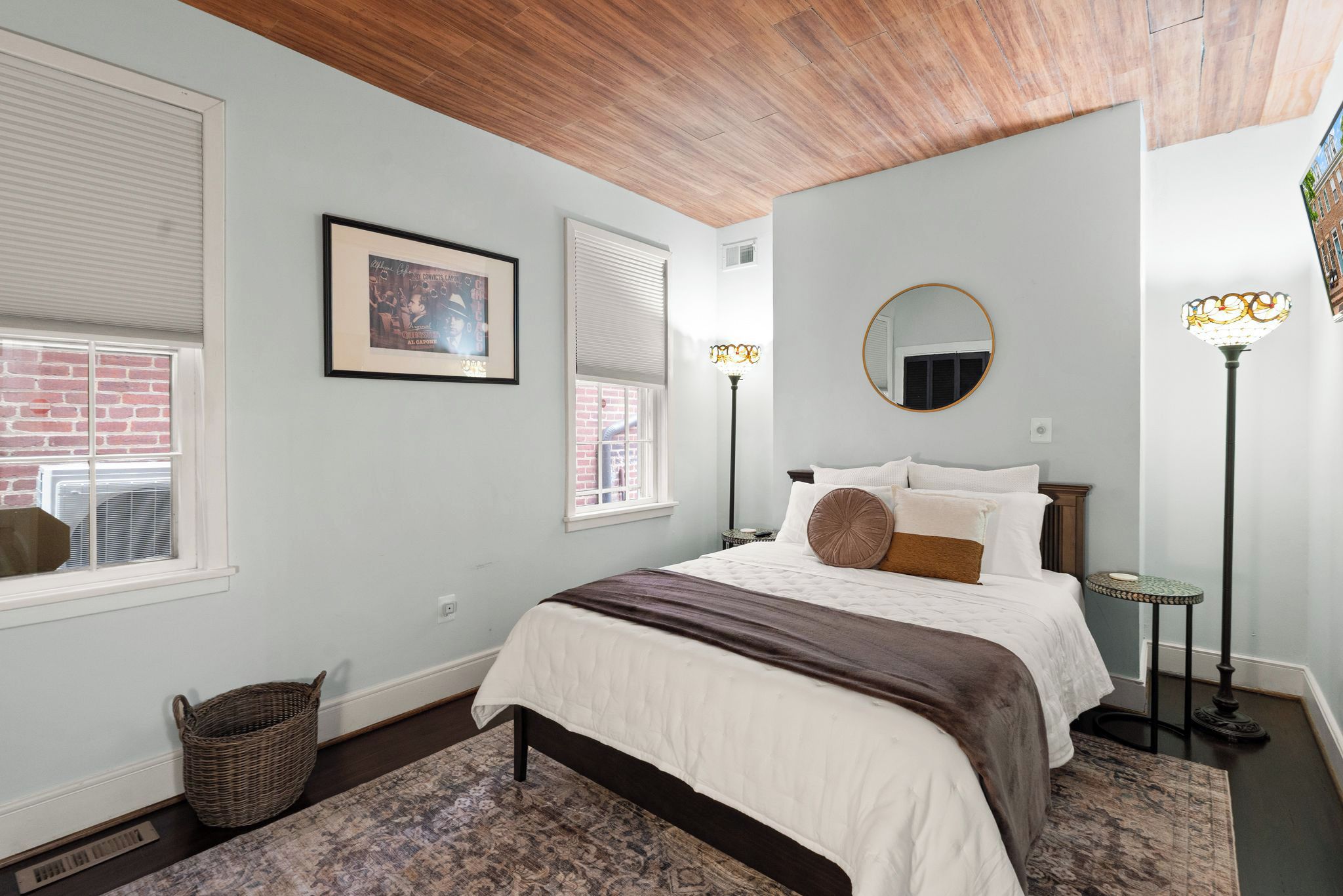 A bedroom with a bed, a framed picture, a round mirror, and a floor lamp.