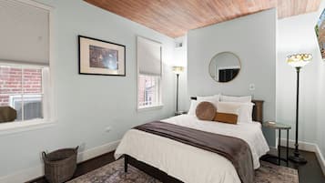 A bedroom with a bed, a framed picture, a round mirror, and a floor lamp.