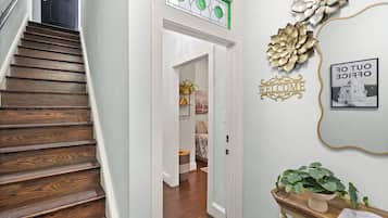A wooden staircase leading to a room with a bed, a wall-mounted welcome sign, and a framed picture.