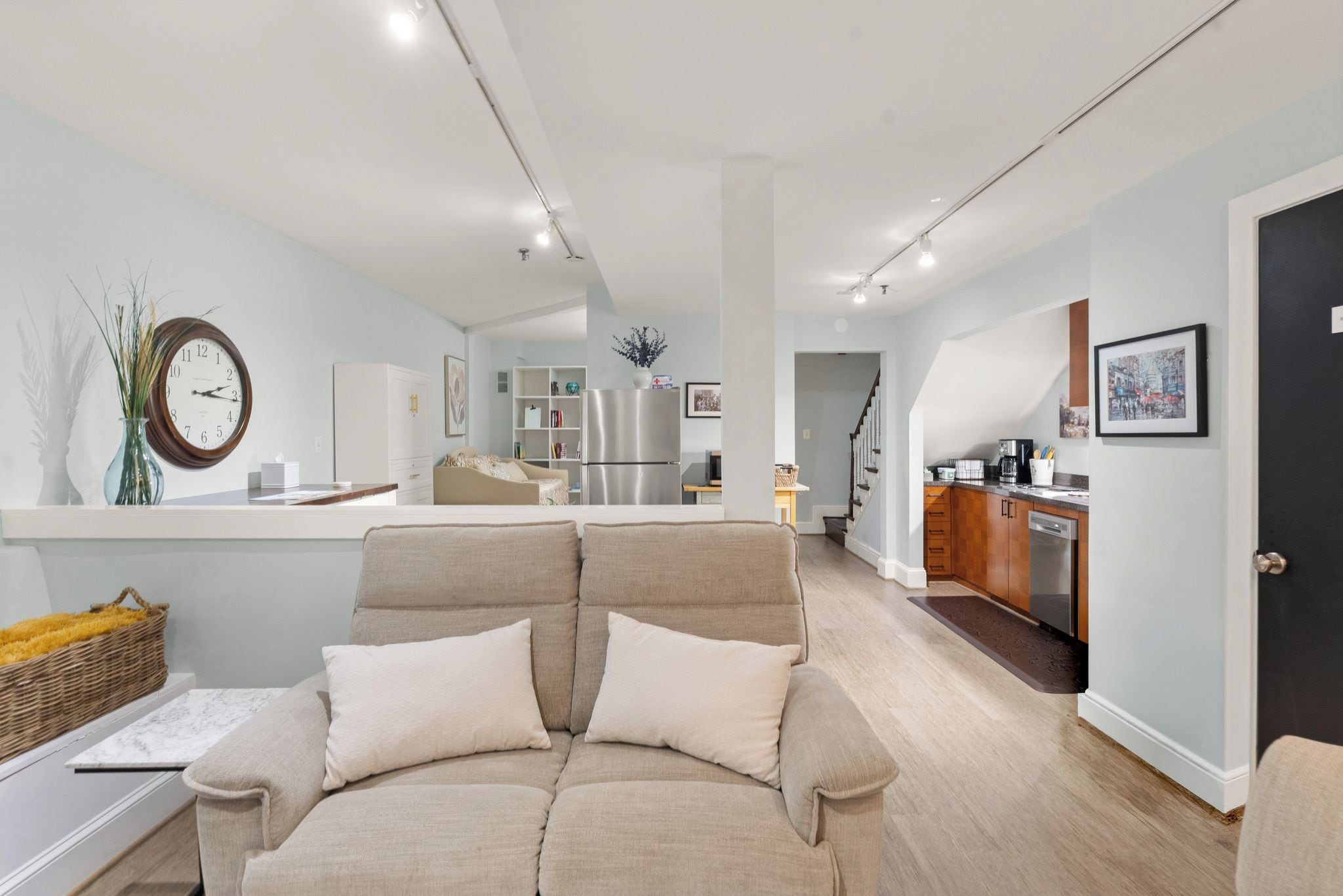 A modern living room with a sofa, a dining area, a kitchen, and a staircase leading to another level.