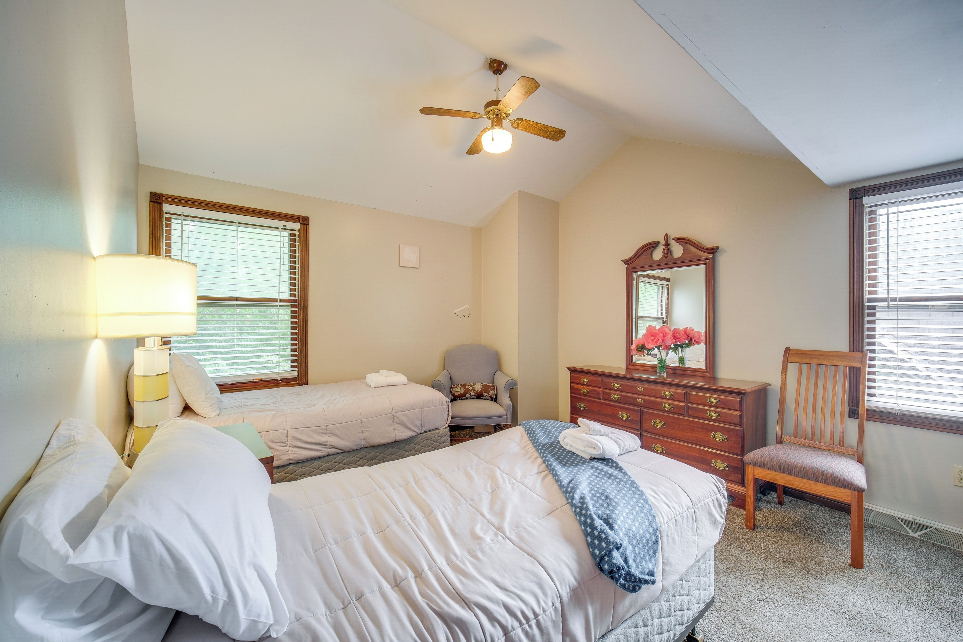 Une chambre d’hôtel avec deux lits, un ventilateur de plafond, une commode, une chaise et une fenêtre avec des stores.