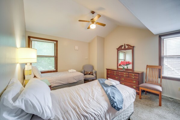 A hotel room with two beds, a ceiling fan, a dresser, a chair, and a window with blinds.