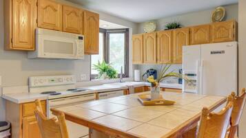 Une cuisine avec des meubles de rangement en bois, un four à micro-ondes, une cuisinière, un réfrigérateur et une table à manger avec des chaises.