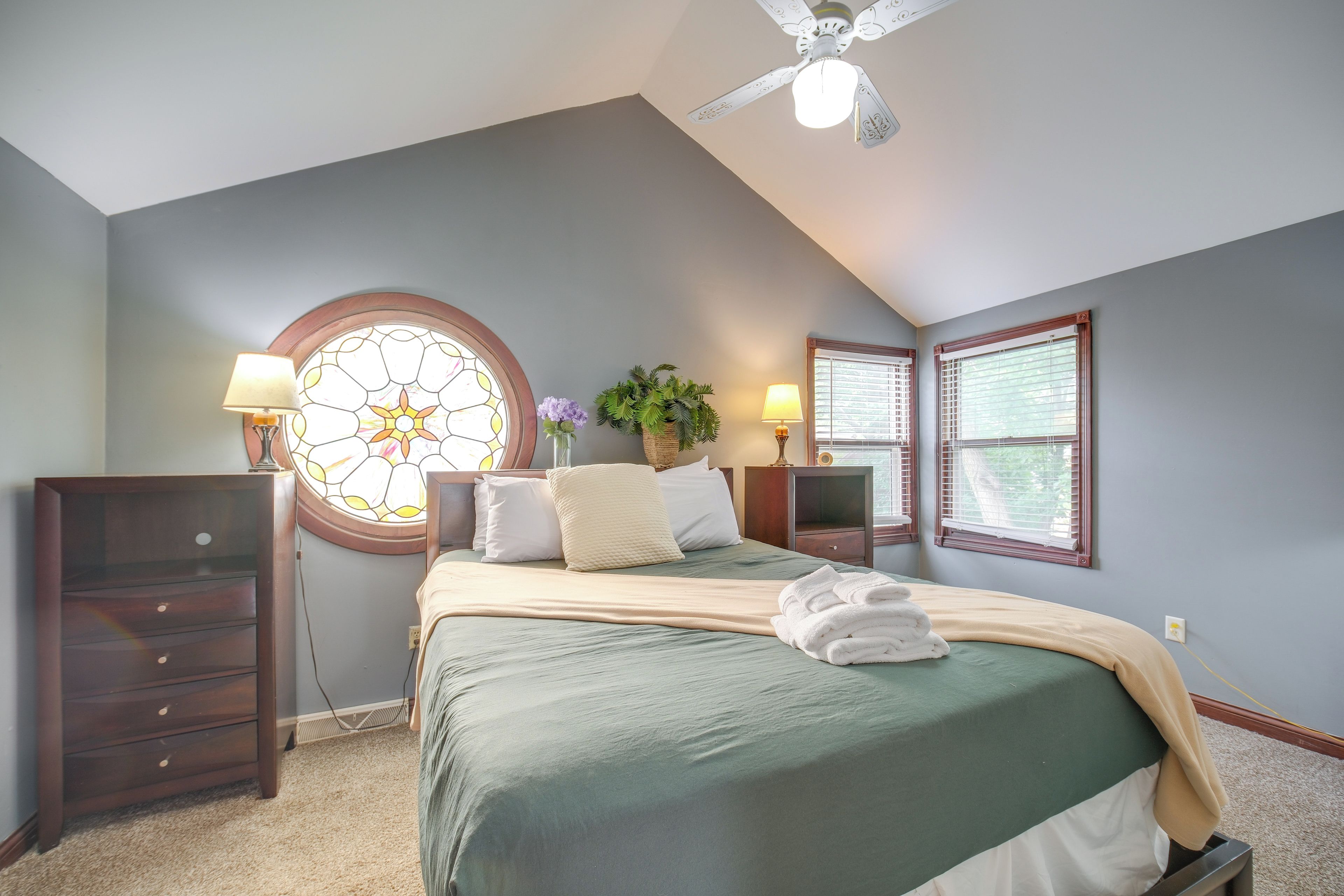 A bedroom with a bed, a dresser, a nightstand, a lamp, a window, and a ceiling fan.