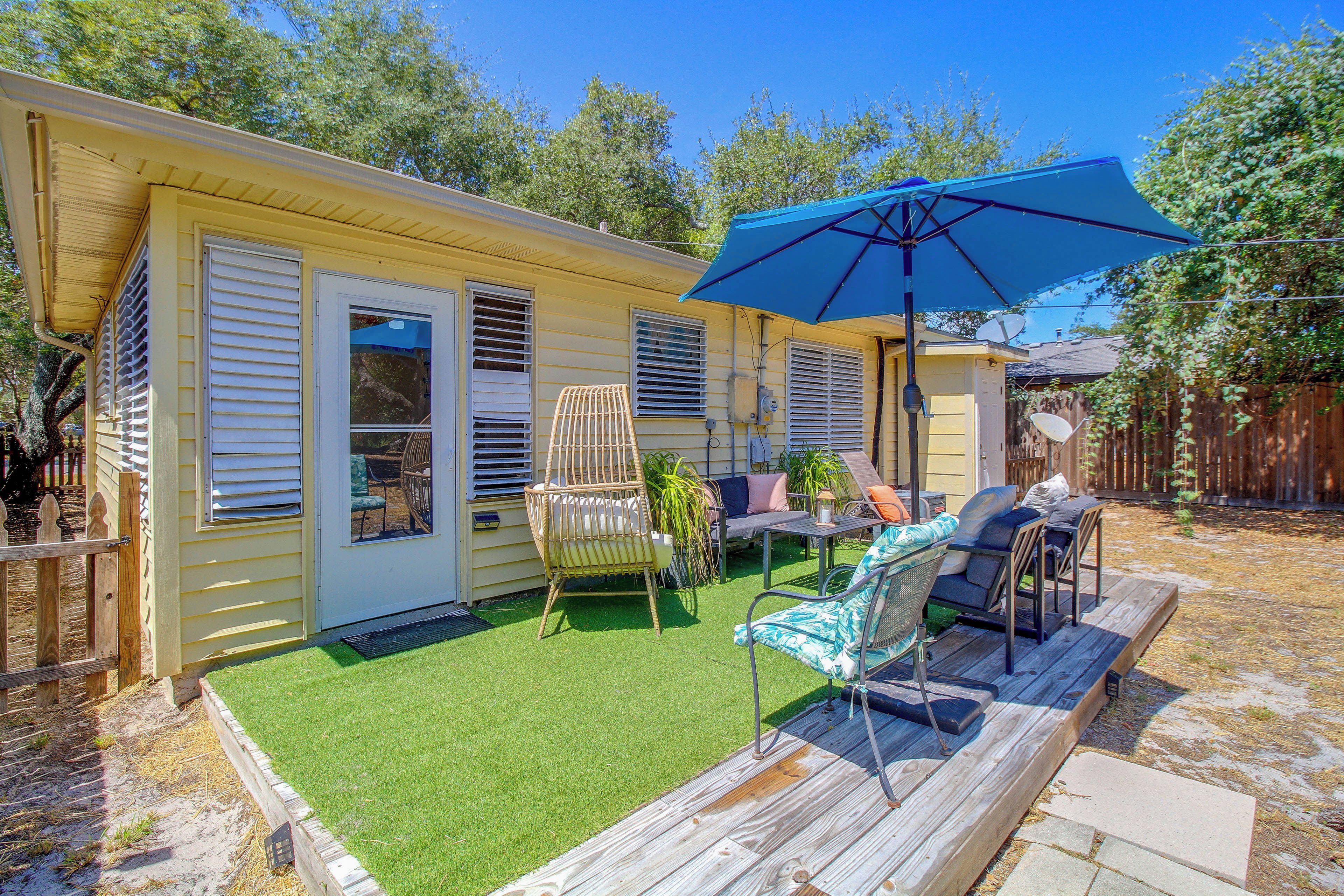 A mobile home with a patio area featuring outdoor furniture, a blue umbrella, and a small lawn.