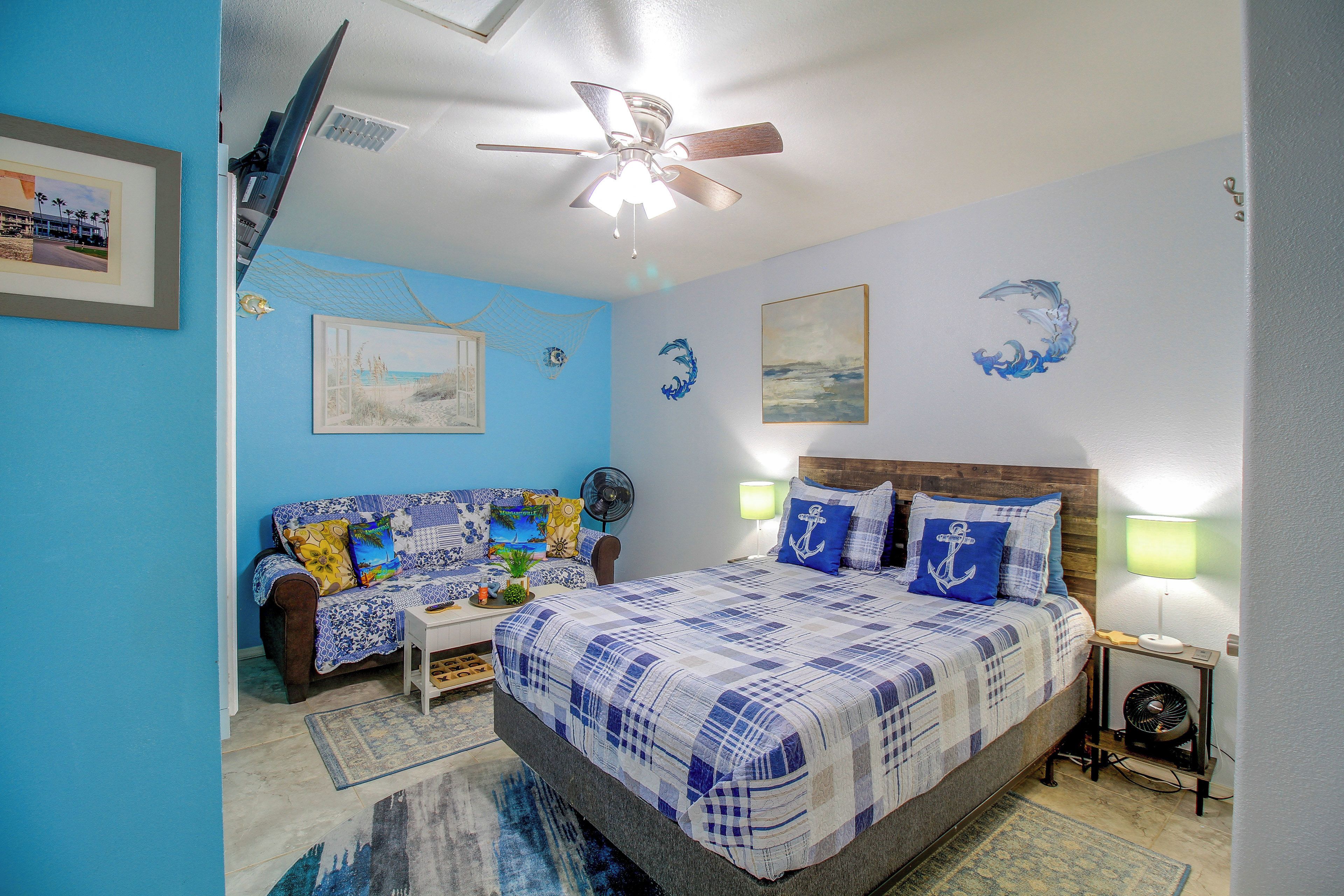 A bedroom with a bed, a sofa, a ceiling fan, and wall art.