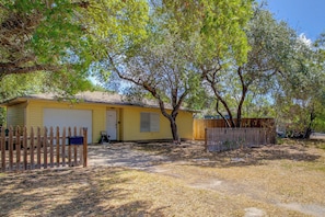 A single-story yellow house with a garage, surrounded by a wooden fence, and trees in the background. - Little Minnow - Just Minutes From the Water (Aransas Pass)