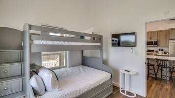 A bunk bed with a desk and drawers, a television on the wall, and a kitchen area with a microwave and stools.