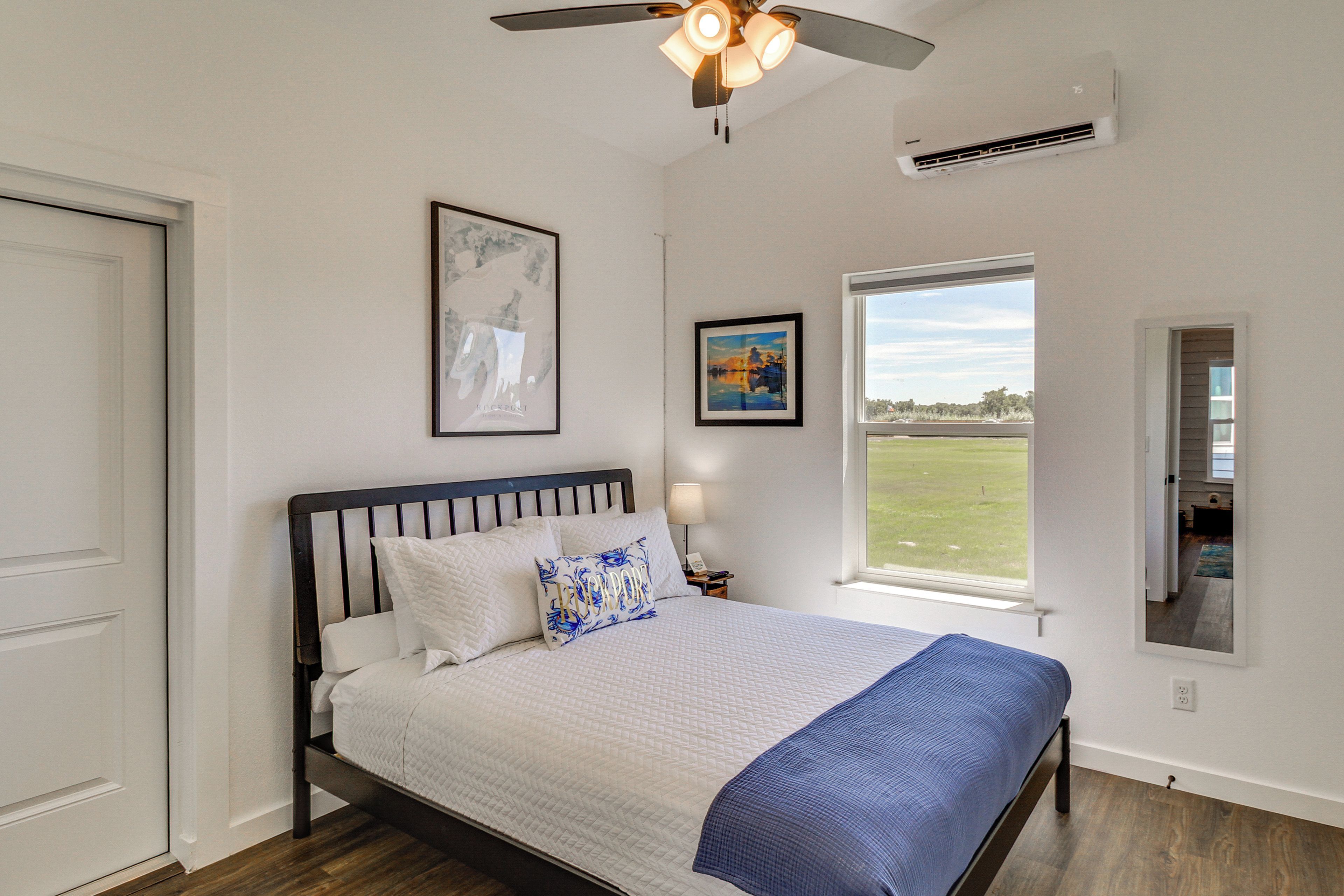 Un dormitorio con cama, ventilador de techo, ventana con vistas y cuadros en la pared.