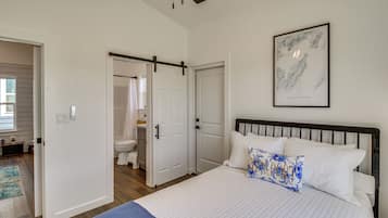 A bedroom with a bed, a bathroom with a toilet and shower, and a door leading to another room.