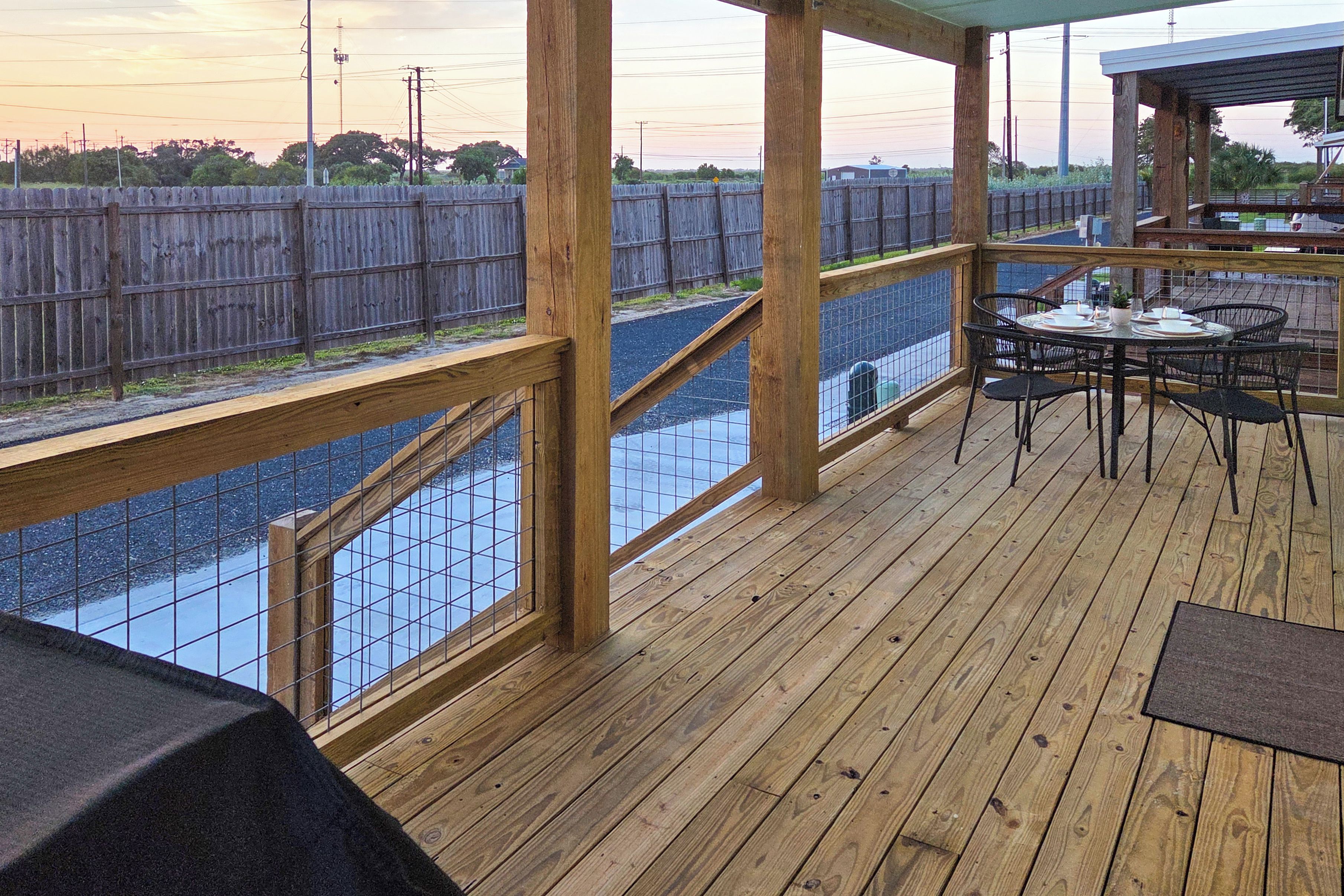 Una terraza de madera con una mesa y sillas, con vista a un área cercada con una masa de agua.